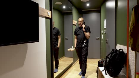 an asian man talking on his mobile phone while pacing up and down a vestibule of a hotel room