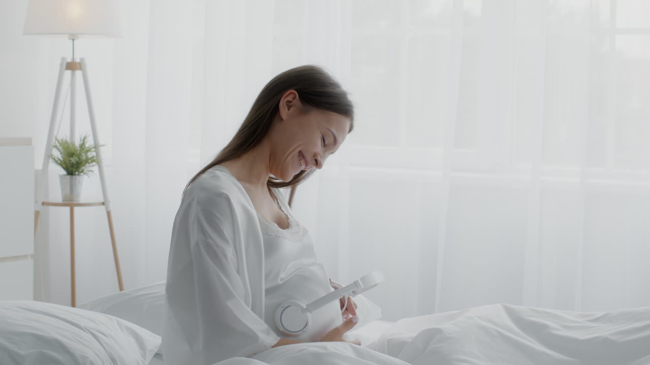 임신 한 여자 가 침대 에서 음악 을 듣고 있다