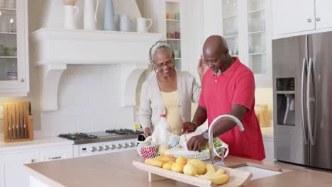 Feliz-Pareja-De-Ancianos-Afroamericanos-Desempacando-Comestibles-En-La-Cocina,-Cámara-Lenta