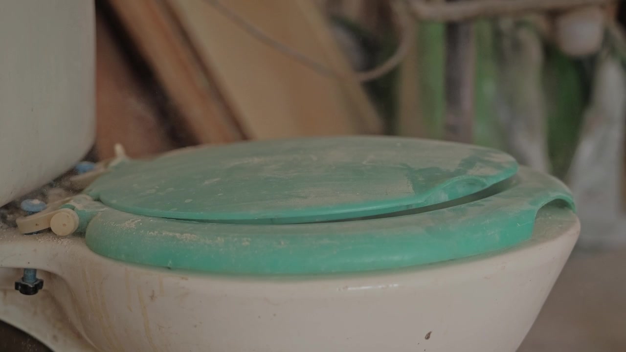 Slow motion of dusty toilet lid closing as fine renovation debris fills air