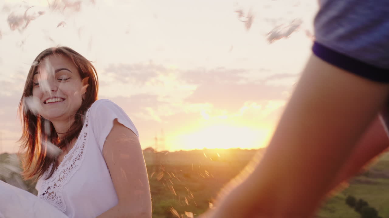 젊은 사람들은 미친 듯이 즐겁게 지내고 있다 한 여자는 친구와 함께 베개를 때리고 있다 깃털이 날고 있다