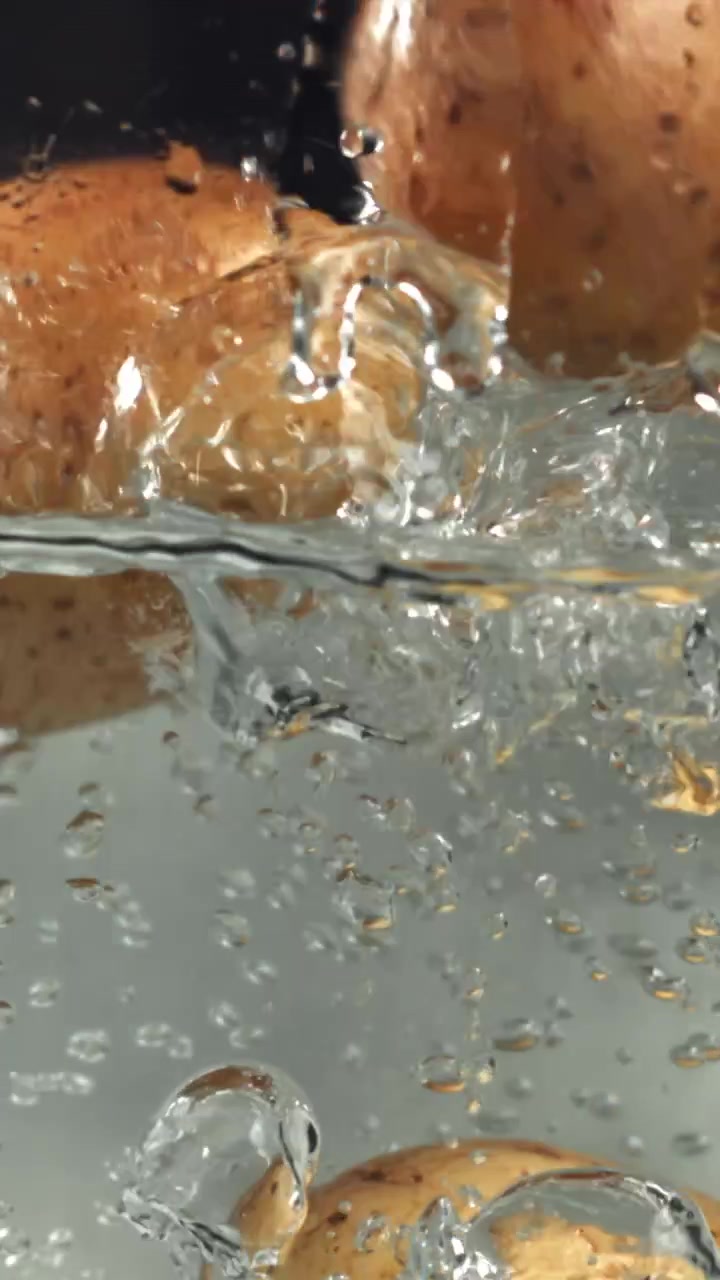 Patate fresche che si tuffano in acqua limpida al rallentatore