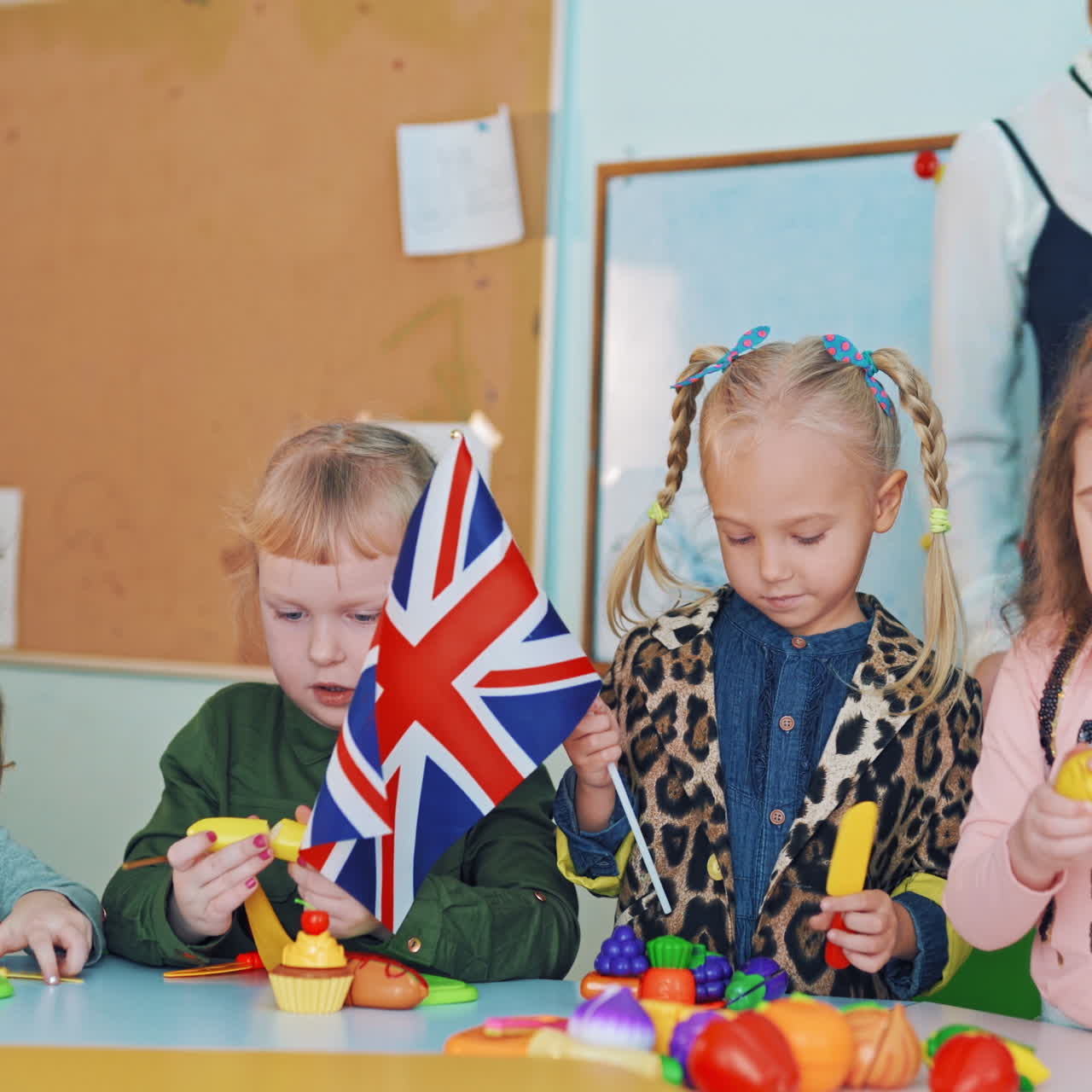Positive kids with flags at during the lesson. Little children playing with fruit patterns and waving flags. British and German flags in girls hands.