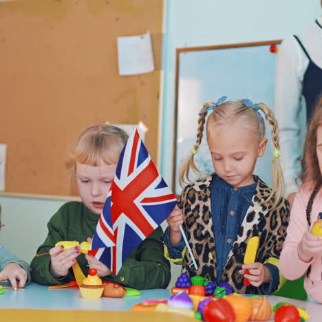 positive kids with flags at during the lesson. little children playing with fruit patterns and waving flags. british and german flags in girls hands.