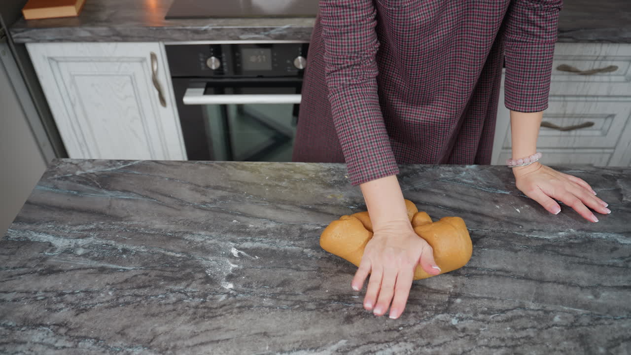 左手にブレスレットをかぶった女性がキッチンカウンターに横たわり右手で新鮮な生地をみ背景にキャビネットを備えたキッチンセット