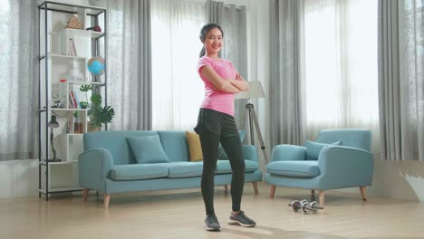 una chica asiática en ropa deportiva está posando con una suave sonrisa en su sala de estar.