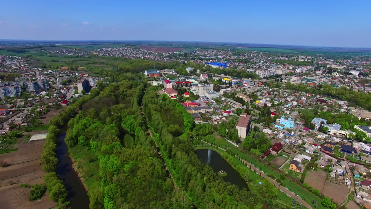 Cityscape with river and lots of trees on sunny day. Clear blue sky at backdrop. Aerial perspective.