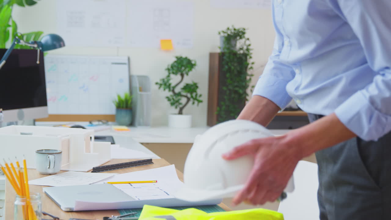 arquitecto masculino en la oficina de vuelta de la visita al sitio trabajando en planes para un nuevo edificio usando una computadora portátil