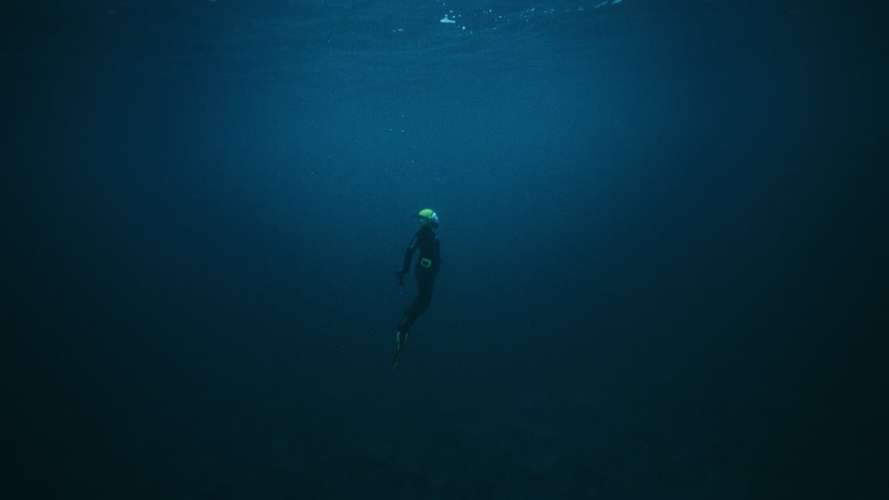 Lone diver floating in dark Arctic Ocean water column above rocky seabed
