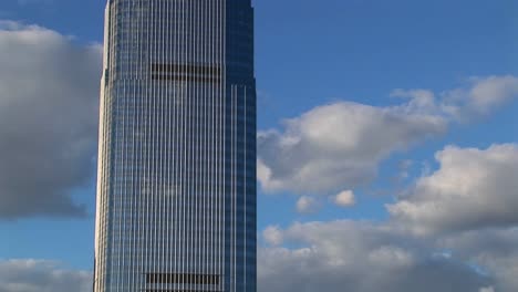 a time lapse of clouds moving across a blue sky behind a tall and reflective skyscraper in hoboken new jersey