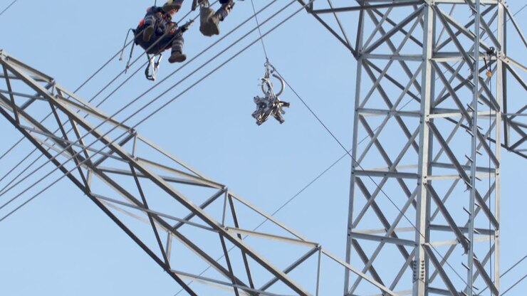 Two workers sit on high power voltage cables hoist equipment up