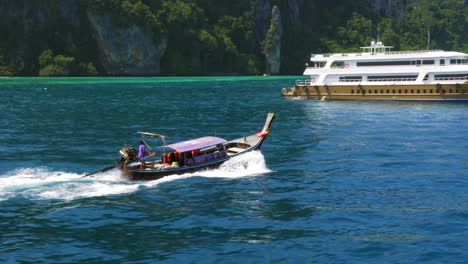 a traditionally designed tourist boat taking people back to the beach of thailand, passing a tourist yacht - wide rolling