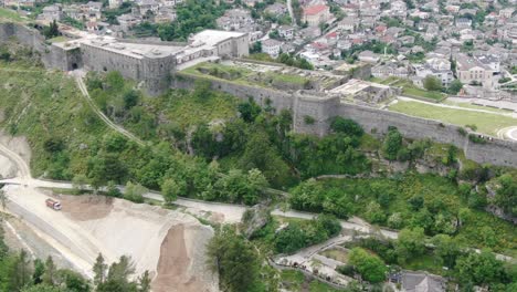 Drone-view-in-Albania-flying-in-Gjirokaster-town-over-a-medieval-castle-on-high-ground-fort-showing-the-brick-brown-roof-houses