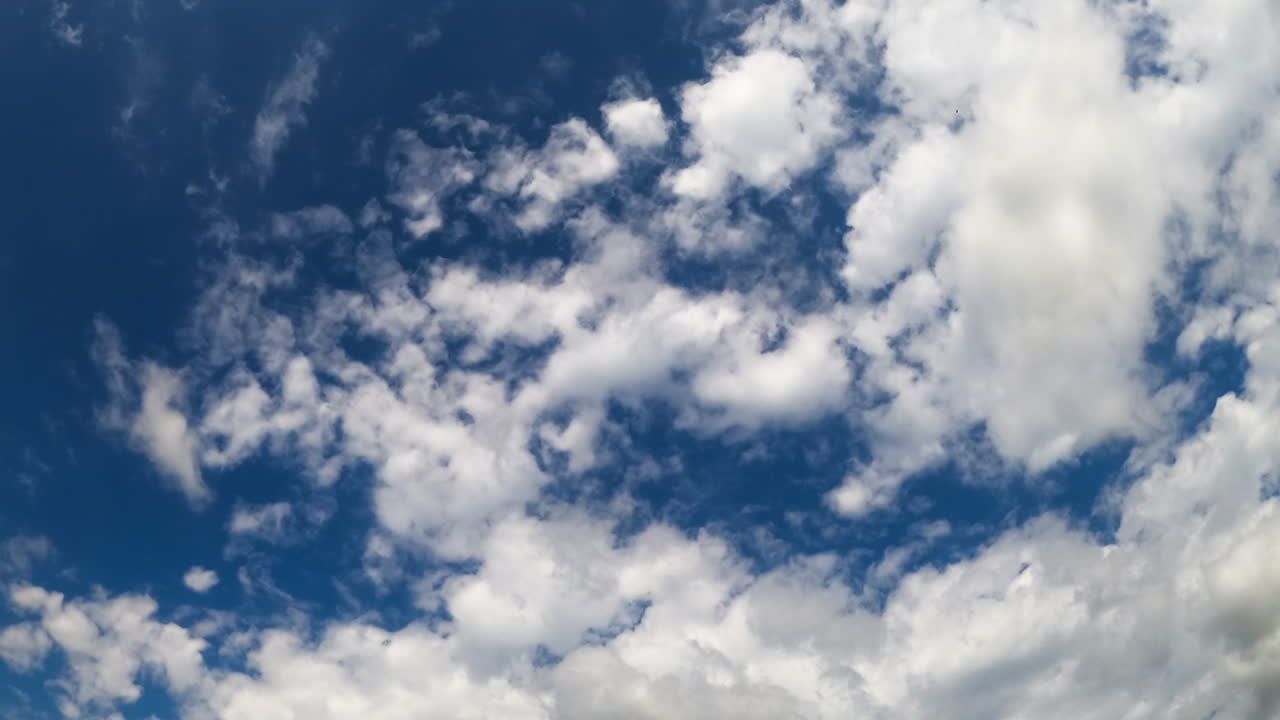 Groups of clouds move in two directions crossing in the atmosphere. Dark blue sky with transforming cloudscape. Low angle view. Timelapse.