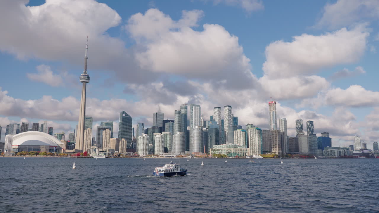 Barca che naviga sul Lago Ontario con lo skyline di Toronto sullo sfondo, ampia veduta del moderno paesaggio urbano e del lungolago sotto nuvole drammatiche.