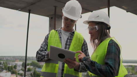 trabajador de la construcción hombre y arquitecto mujer en un casco discutir el plan de construcción de la casa hablar el uno al otro sobre el diseño sosteniendo una tableta mirar los dibujos fondo de los rayos del sol.