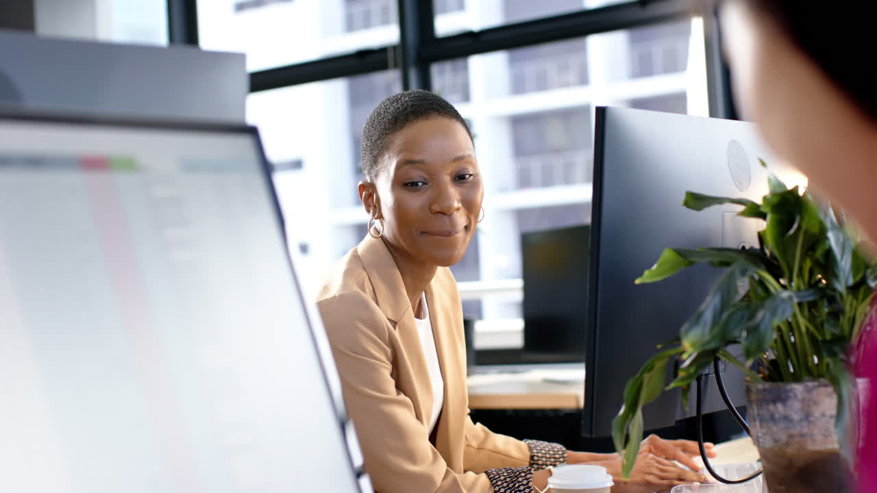 Portrait of smiling african american businesswoman by computer in office, slow motion, copy space
