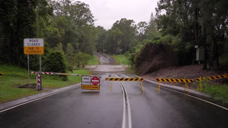 gold coast, queensland, 16 february 2024 - wide shot of road closure signage with flooding across hardy's road in mudgeeraba after heavy rains continue to lash south east queensland, australia