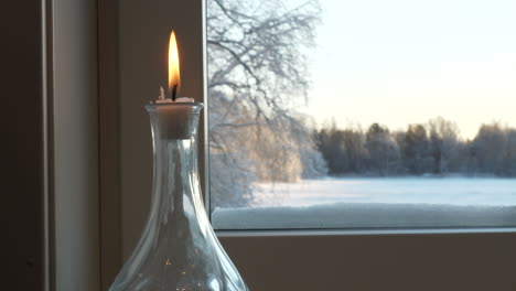 interior view of candle burning in window with snowy winter landscape outside