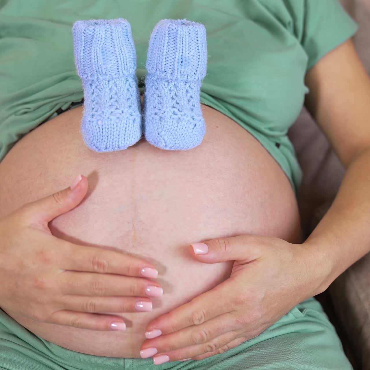 Futura mamma accarezza il suo pancione. Calzini a maglia blu su una pancia nuda di una donna incinta. Salute della donna e benessere delle persone. Assistenza prenatale per la maternità