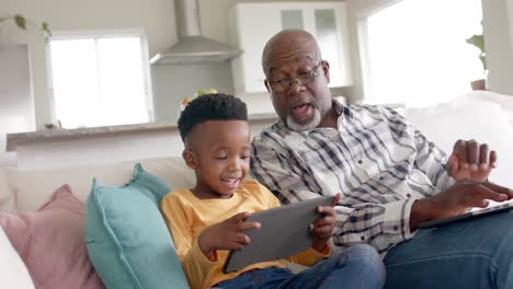 African-american-grandfather-with-grandson-using-tablet-on-couch-at-home,-slow-motion