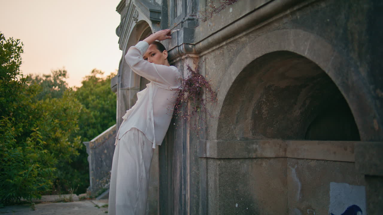 오래된 벽에 기대어있는 고대 건물을 포즈하는 화려한 모델. 성을 포지션하는 여성