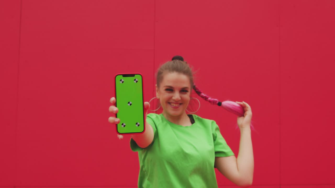 sonriente joven feliz mostrando teléfono con clave de croma pantalla verde con puntos de seguimiento, divirtiéndose. video publicitario