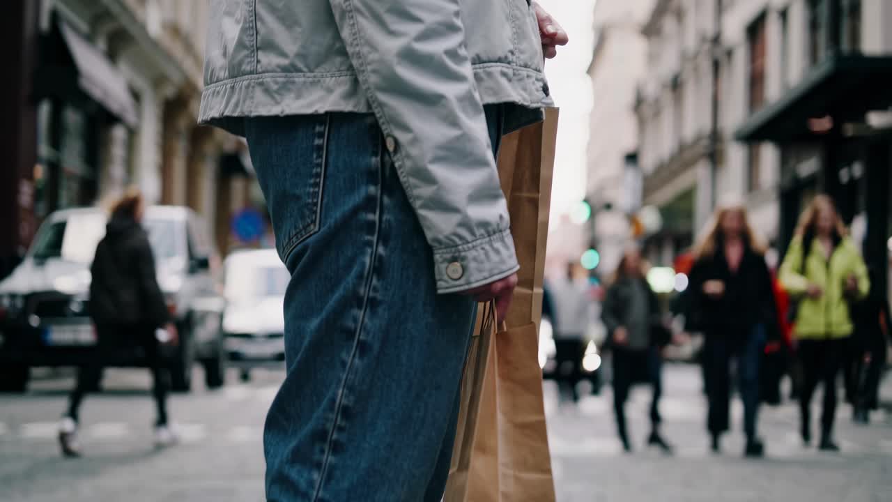 Street-level video captures a person holding a shopping bag, focusing on casual urban fashion amidst