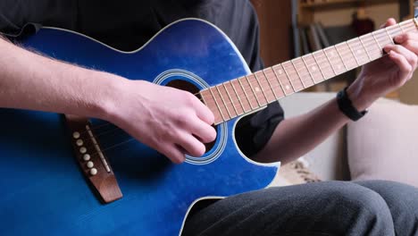 A male musician plays a blue acoustic guitar. Modern young hipster guitarist playing guitar. Stylish curly hair.