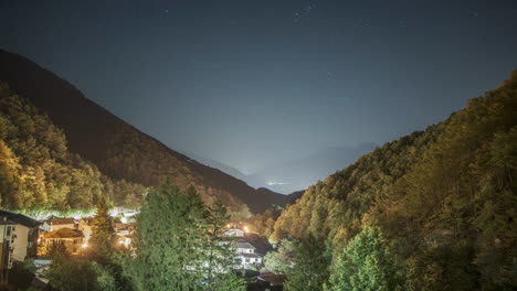 Vista-Nocturna-De-Un-Pueblo-De-Montaña-Bajo-Un-Cielo-Estrellado,-Luces-Brillando-Cálidamente-Entre-Los-árboles,-Lapso-De-Tiempo