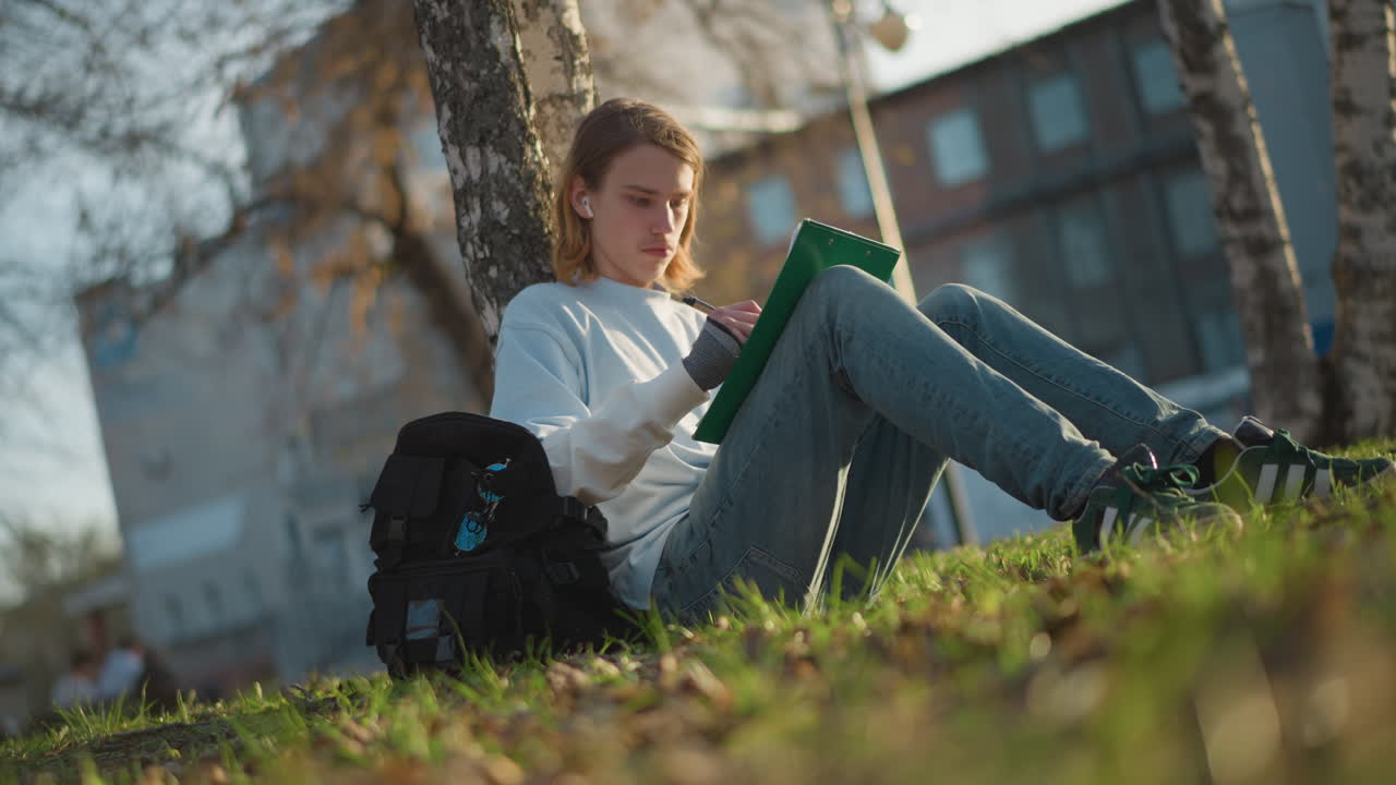 조용한 저녁에 자작나무 옆에서 그림 그리기에 몰두한 학생이 조용히 스케치를 하고 있어요. 평온한 늦은 오후, 나무 근처에서 예술 작품을 열심히 만드는 젊은 예술가의 모습입니다.