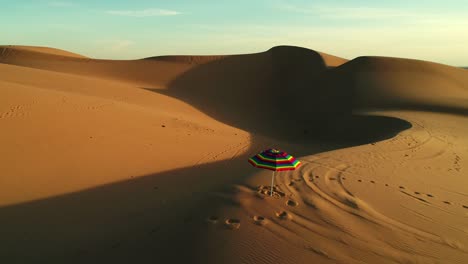 aerial fly by of colorful beach umbrella isolated in desert sand dunes at sunset