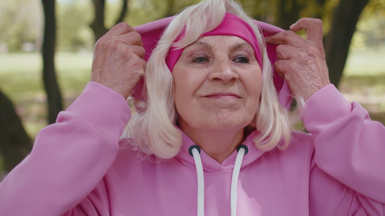 Portrait of athletic senior sport runner woman training, listening music in earphones, wearing hood