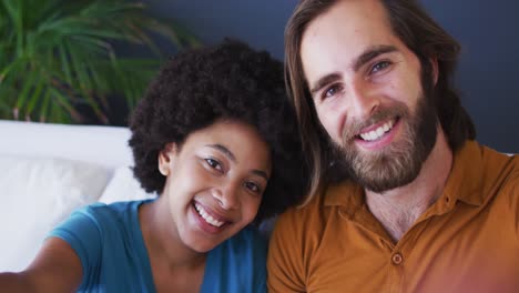 retrato de una pareja de razas mixtas tomando una selfie mientras están sentados en el sofá en casa