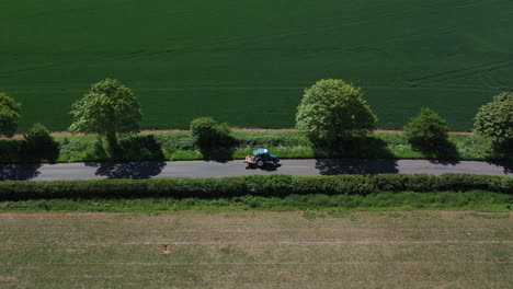 Aerial-shot-of-a-small-blue-tractor-driving-down-the-road