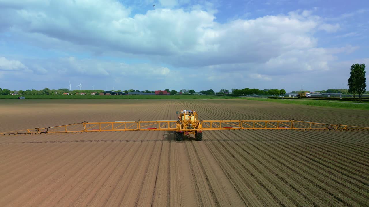 Drone follows a farmer in a tractor spraying the field with crop protection products on a partly cloudy day