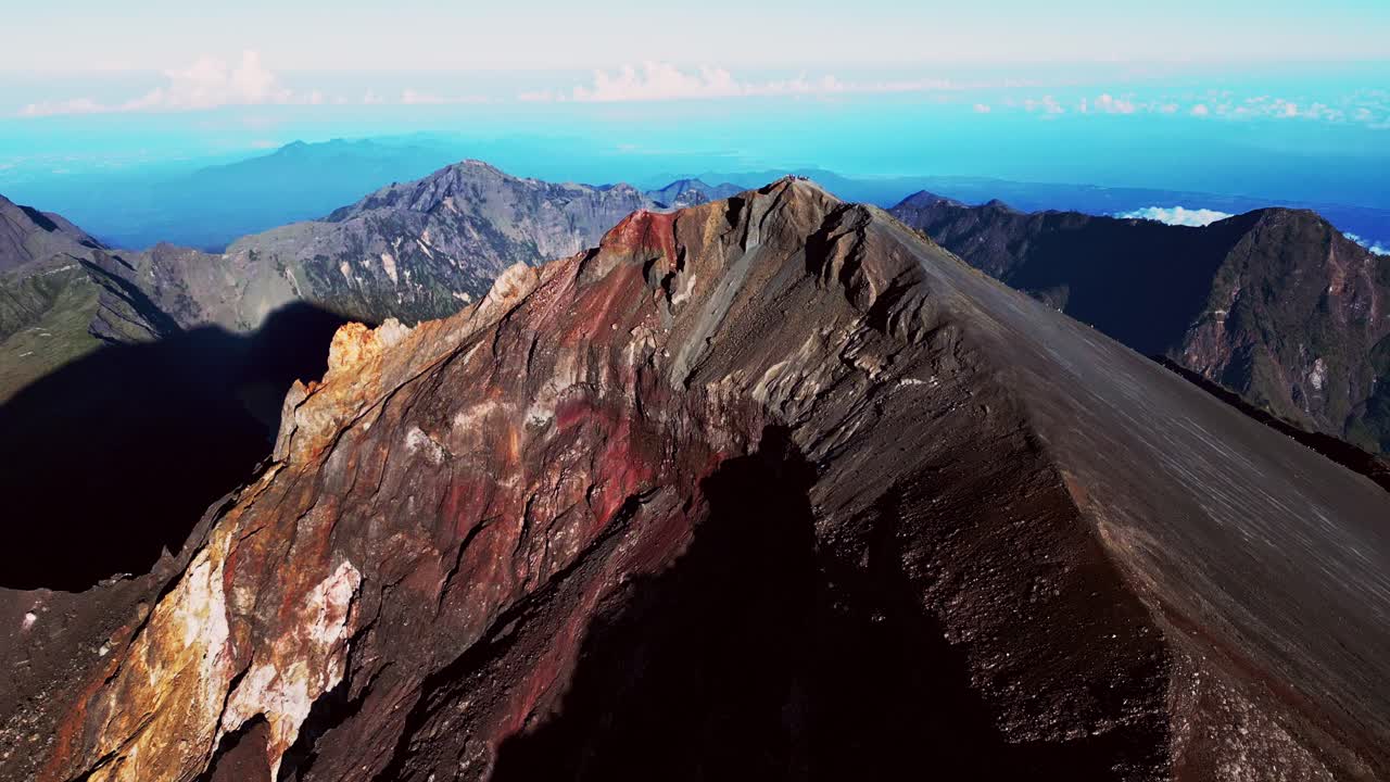 High altitude drone view of hikers celebrating on top of Mount Rinjani during golden morning light.