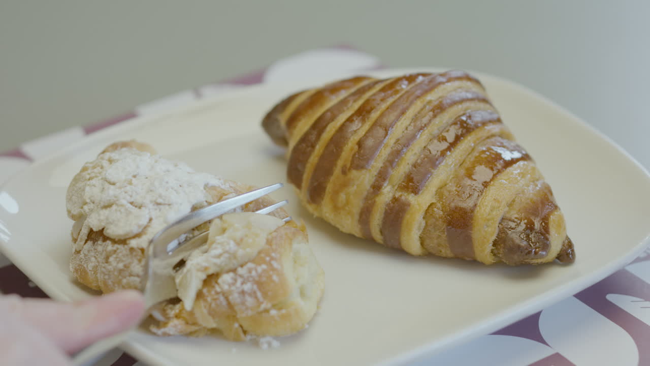 Close-up of a sweet croissant glazed and sprinkled with icing sugar, while a fork cuts a portion showing its crispy and soft texture