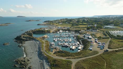 Flight-over-Beaucette-Marina-flying-south,-north-east-coast-of-Guernsey-on-bright-sunny-day-showing-marina-built-in-an-old-quarry-and-views-over-Herm,-Jethou-and-Sark-and-further-out-to-sea