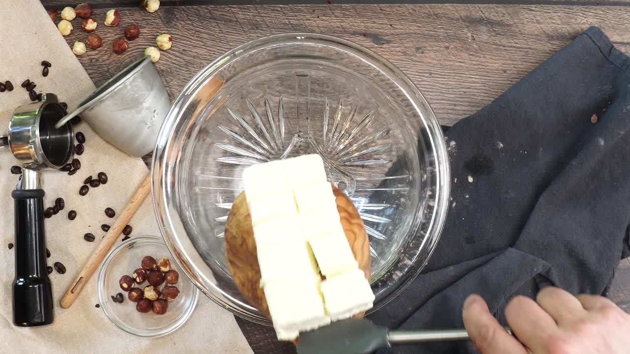 A delicious dessert, Coffee Hazelnut Cream Tart. Made with espresso powder, chocolate crust and loaded with crushed hazelnut. Adding softened butter to a clear mixing bowl on a wooden table