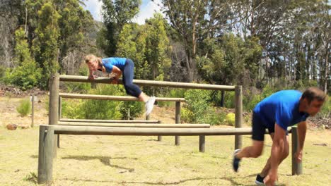 fit man and woman climb a hurdles during obstacle course