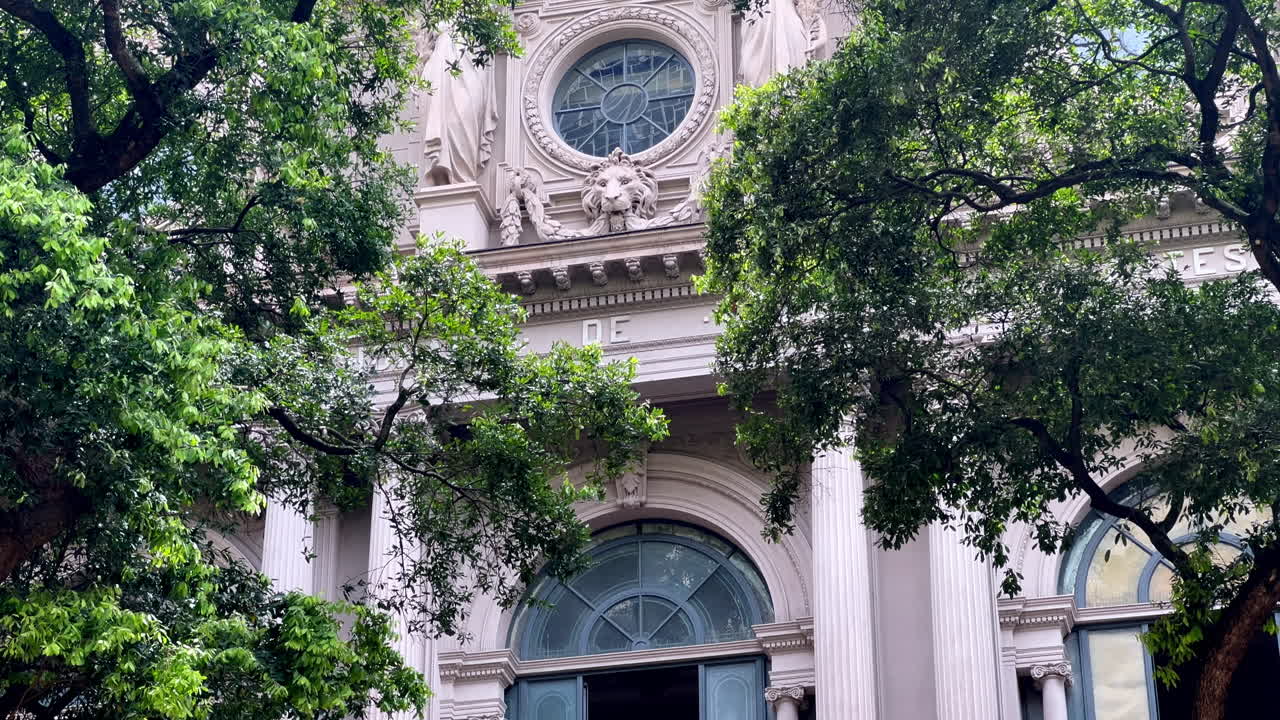 Inclinación vertical descendente de la fachada del Museo Nacional de Bellas Artes. Capta detalles neoclásicos ornamentados, esculturas de leones de piedra y ventanas arqueadas enmarcadas por exuberantes árboles verdes en Río