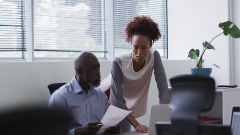 Diverse-businessman-and-businesswoman-talking-and-using-laptop-in-office