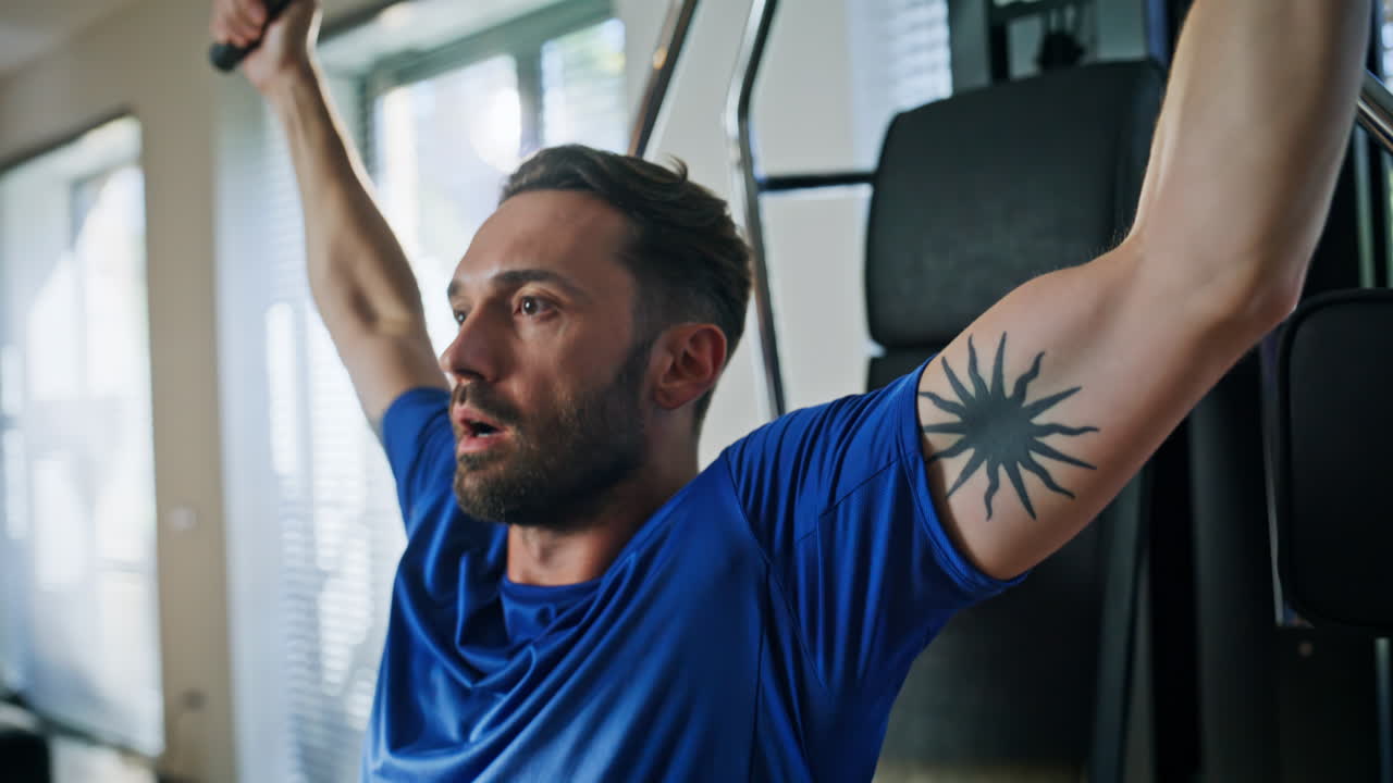 Mand pumper bicepsmaskine for træning tæt på. Stærk sportsmand træner i fitnesscenter