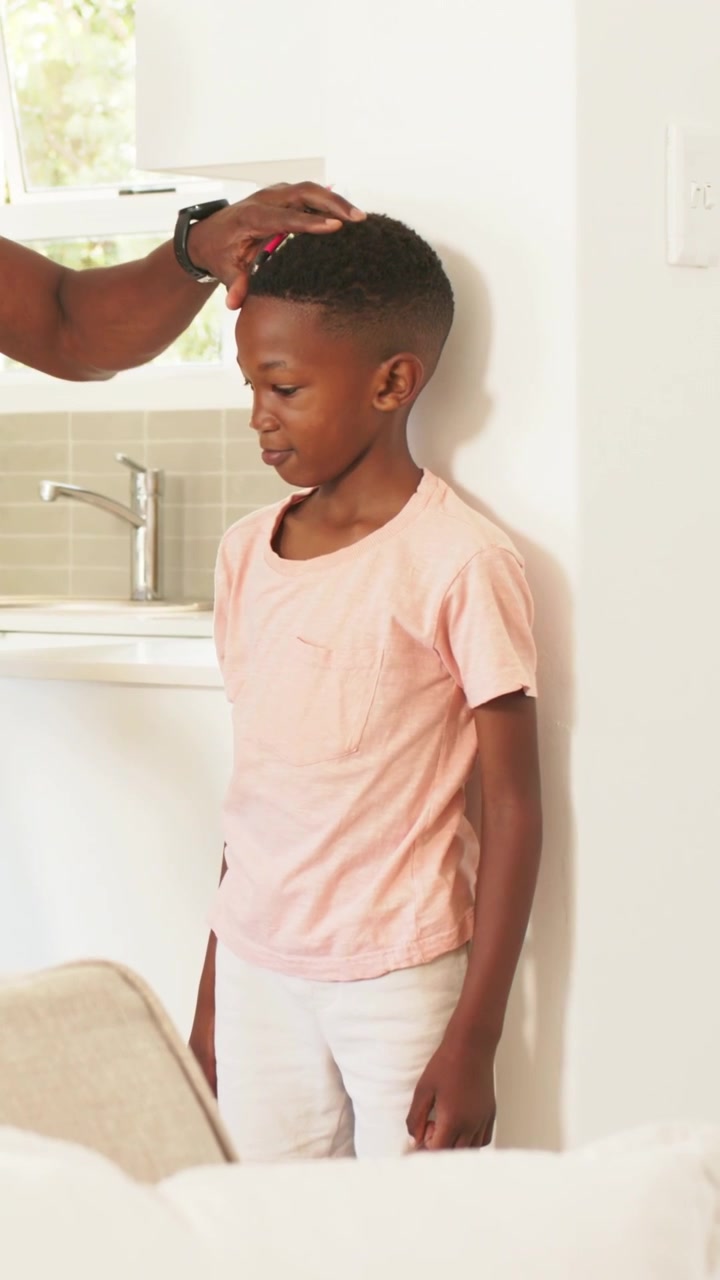 Vertical video: Guiding dad touching shoulder, measuring child's height in kitchen with yellow tape