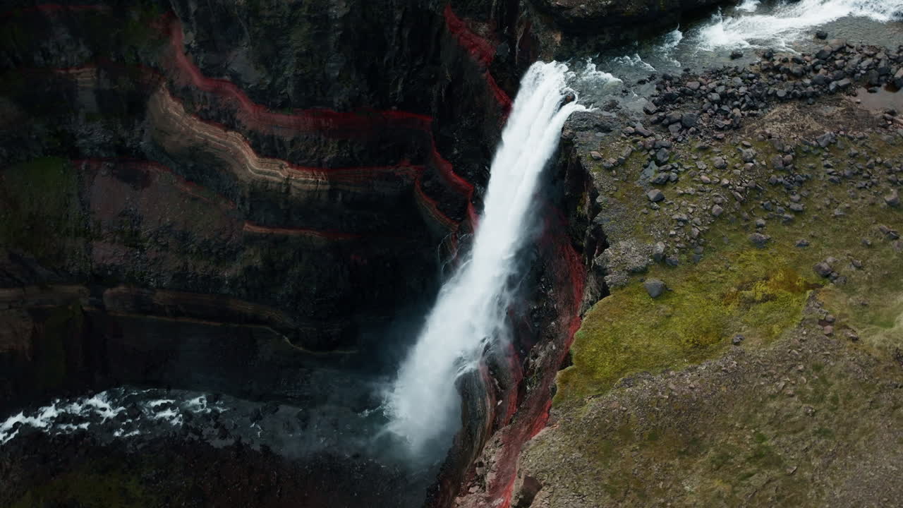 Close up aerial drone shot of Hengifoss Waterfall in motion, Iceland, sunny day, green grass, red clay. Part 7.