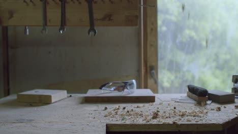 Person-is-pouring-down-wood-sawing-remains-on-the-table-in-workshop,-safety-glasses-and-other-tools-visible,-hand-manufacturing-and-DIY-concept