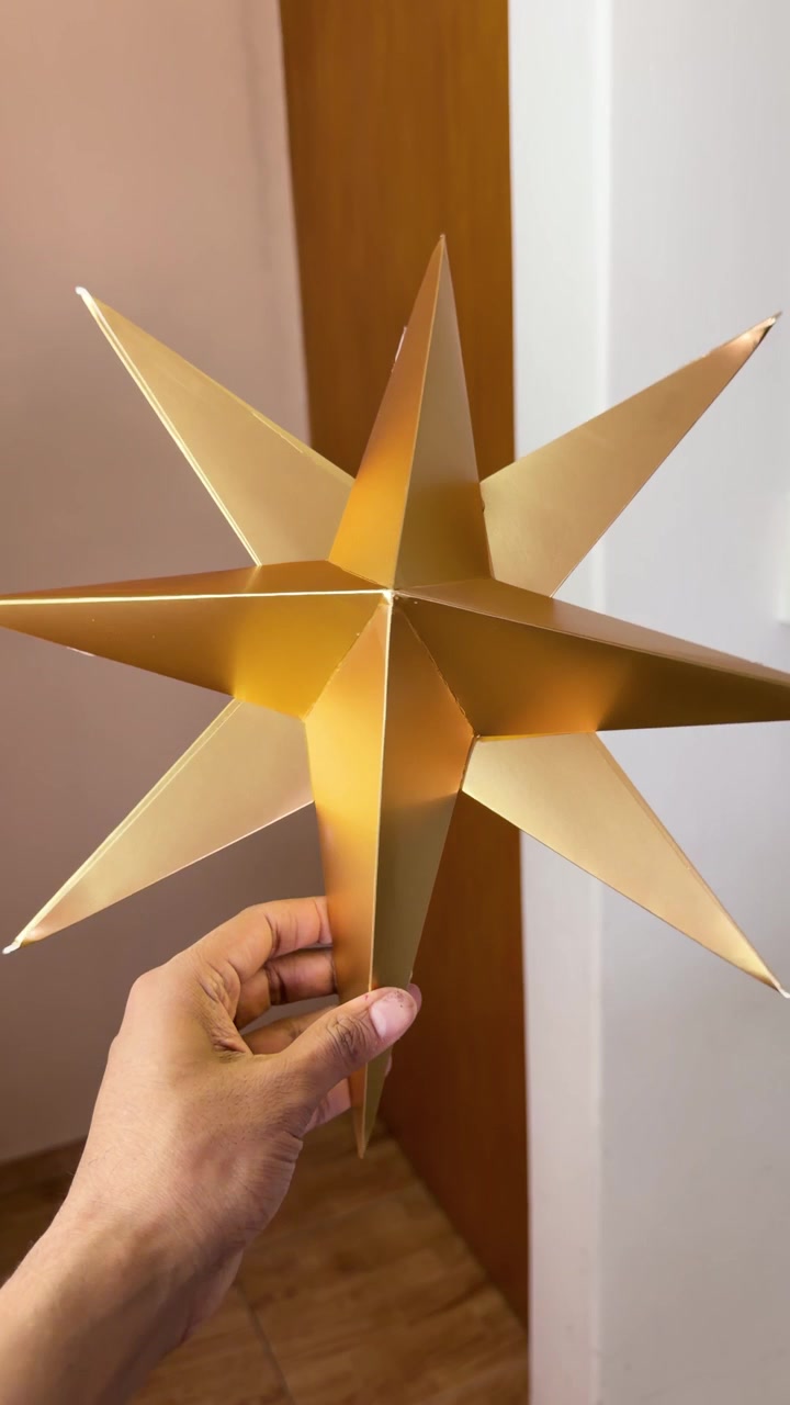 Mano che tiene una decorazione a stella di Natale 3D color oro metallizzato al chiuso, che ruota per mostrare la pregevole fattura, verticale.