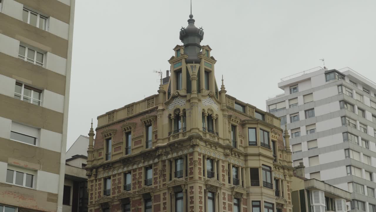 Impresionante edificio histórico ornamentado en Gijón, España, con una elaborada arquitectura Belle Époque y una torre de corona decorativa contra un cielo nublado.