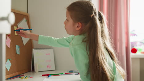 calm girl takes off cap from felt-tip pen sitting at desk